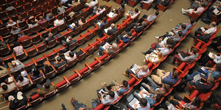 Foto: Sitzreihen mit vielen Personen in einem Konferenzsaal von oben betrachtet